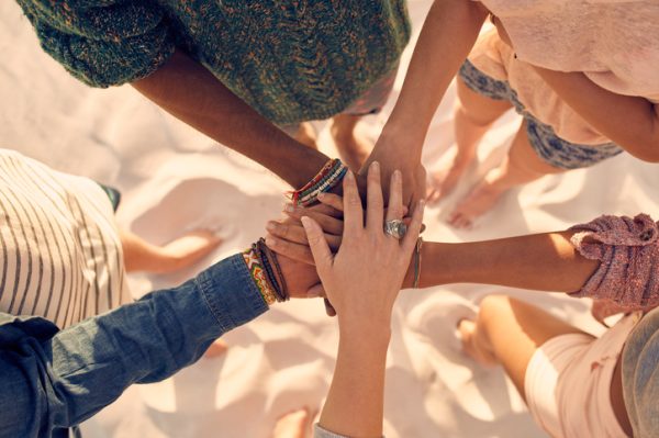 Young men and women showing unity Group of young men and women showing unity. Group of young friends putting their hands together at the beach.