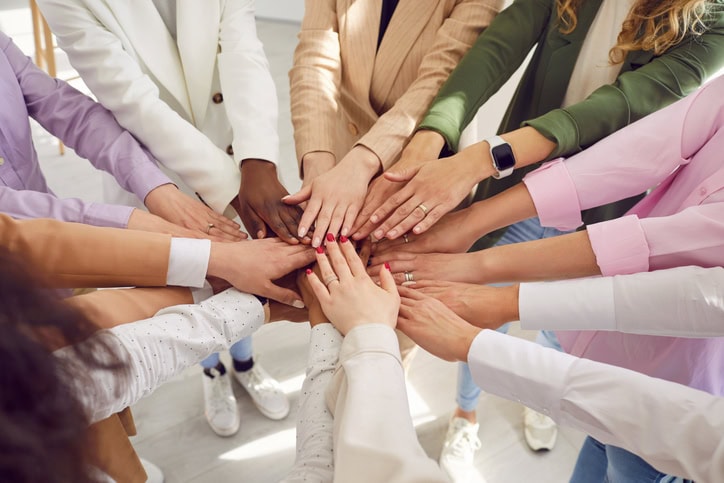 Team of young, diverse, mixed race, multiethnic business women all together holding their hands with different skin colors in a circle. Teamwork, support, unity, cooperation, success concepts