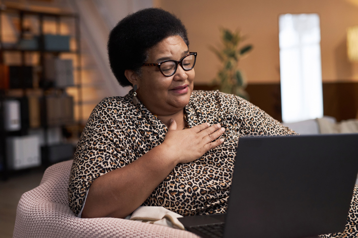 Portrait of smiling Black senior woman enjoying evening entertainment watching movies online via laptop copy space