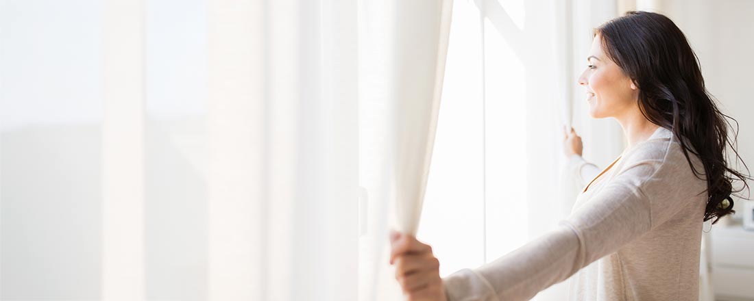 brunette-opening-white-curtains-iStock-868535762@1100x440